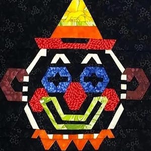 Może przedstawiać: Kolorowa twarz klauna z patchworku na czarnym kwiatowym tle. Klaun ma żółto-pomarańczowy kapelusz, niebieskie oczy, czerwony nos i zielono-pomarańczowy uśmiech. Projekt wykonany jest z różnych wzorów tkanin.