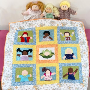 Könnte beinhalten: Eine gelbe und weiße Steppdecke mit einem Blumenmuster. Die Steppdecke hat neun Quadrate, jedes mit einer anderen Applikation eines Kindes. Die Kinder tragen unterschiedlich farbige Kleidung und haben unterschiedliche Frisuren. Die Steppdecke liegt auf einem rosa Bett.
