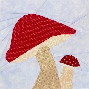 May include: A fabric art piece depicting two mushrooms. The larger mushroom has a red cap with white polka dots, while the smaller one has a red cap with white stars. The stems are tan and beige with a light blue background.