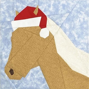 May include: A fabric art piece featuring a horse's head wearing a red and white Santa hat. The horse is tan with a textured pattern, set against a light blue background. The design is geometric, with sharp angles and clean lines, creating a festive holiday theme.