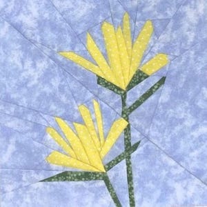 May include: A fabric art piece depicting two stylized yellow flowers with green stems and leaves against a pale blue backdrop. The flowers have a layered petal design, and the background has a subtle, textured appearance.