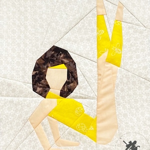 May include: A paper pieced quilt block featuring a stylized figure in a yellow outfit with a brown head and legs raised in the air. The background is a white fabric with a repeating pattern of small white flowers.