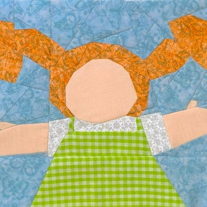 May include: A patchwork quilt block featuring a girl with orange hair, wearing a green and white gingham dress. The background is a light blue with a floral pattern.
