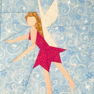 May include: A fabric fairy quilt block. The fairy has a light skin tone, brown hair, and a pink dress with a floral pattern. The fairy's wings are white. The background is light blue with white swirls and star shapes.