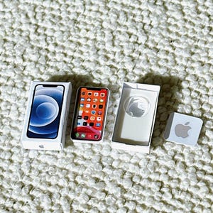 May include: A miniature replica of an iPhone in its original packaging. The phone is white with a black screen and a blue and white background image. The box is white with the Apple logo on the front.