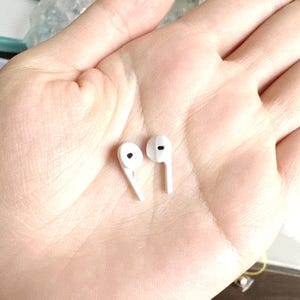 May include: A pair of white wireless earbuds. Each earbud has a rounded top with a small black speaker opening and a long, thin stem. The earbuds are designed to fit comfortably in the ear.