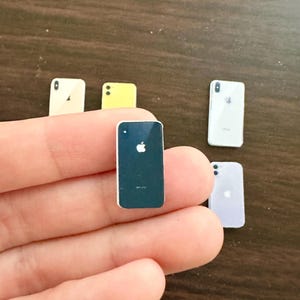 May include: Miniature replicas of smartphones in various colors, including yellow, white, and blue. The phones have a glossy finish and feature the Apple logo on the back. The phones are small enough to be held in a hand.