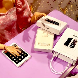 May include: A white iPad tablet with a black screen and a silver border is displayed on a purple surface. The image also shows the tablet's packaging, including a white box labeled "iPad" and a white shopping bag.