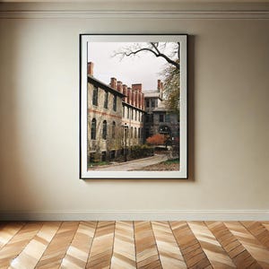 以下が含まれることがあります： 中央に中庭のある石造りの建物の写真。建物には窓が多く、赤いレンガの煙突がある。中庭は木々や茂みで囲まれている。