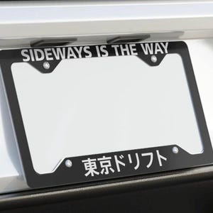 May include: Black license plate frame with the text "SIDEWAYS IS THE WAY" at the top and Japanese text "東京ドリフト" at the bottom. The frame has a white background and is mounted on a vehicle.