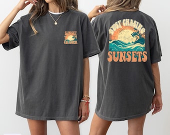 May include: A dark gray oversized t-shirt with a sunset graphic and the text "Sunset Chaser" on the front and "Busy Chasing Sunsets" on the back.