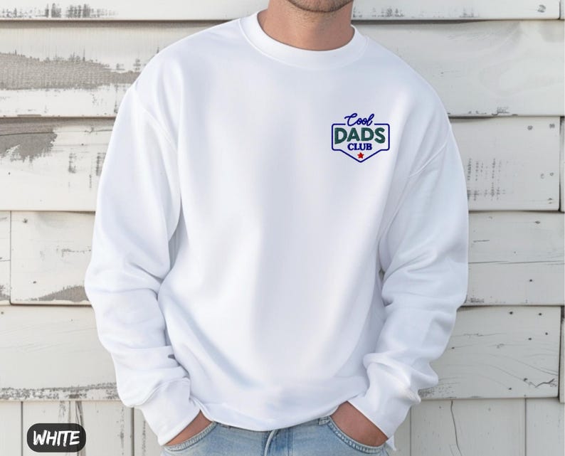 Puede incluir: Sudadera blanca con el texto "Cool Dads Club" en azul y verde en el pecho. La sudadera tiene cuello redondo y mangas largas. La palabra "WHITE" est&aacute; impresa en un recuadro blanco en la parte inferior izquierda.