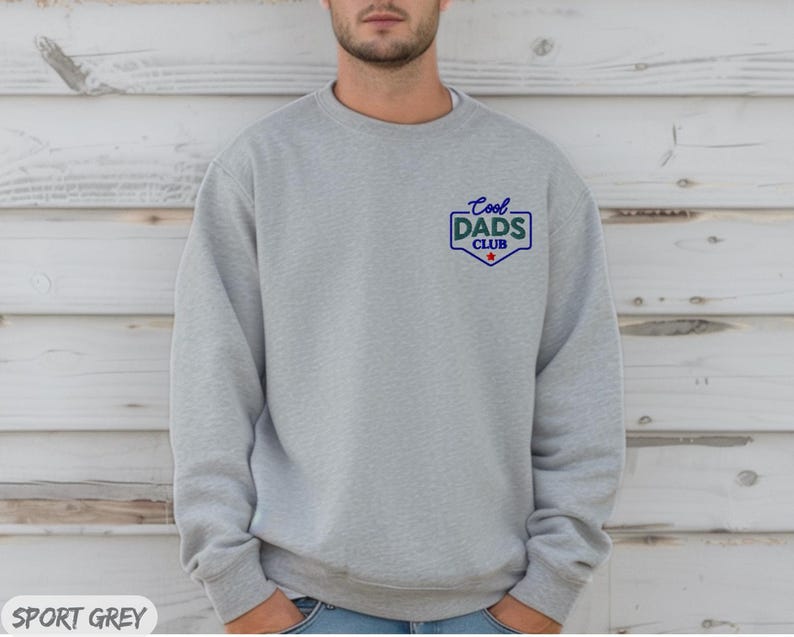 Puede incluir: Sudadera gris deportiva con el texto "Cool Dads Club" en azul y verde en el pecho. El texto est&aacute; dentro de un escudo con una estrella roja. Cuello redondo y mangas largas.