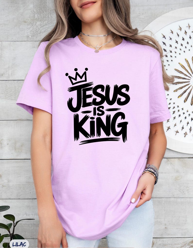 Pu&ograve; includere: T-shirt lilla con la scritta "JESUS IS KING" in nero, con un font a pennello. Il design include una corona sopra la parola "Jesus". La maglietta &egrave; a maniche corte.