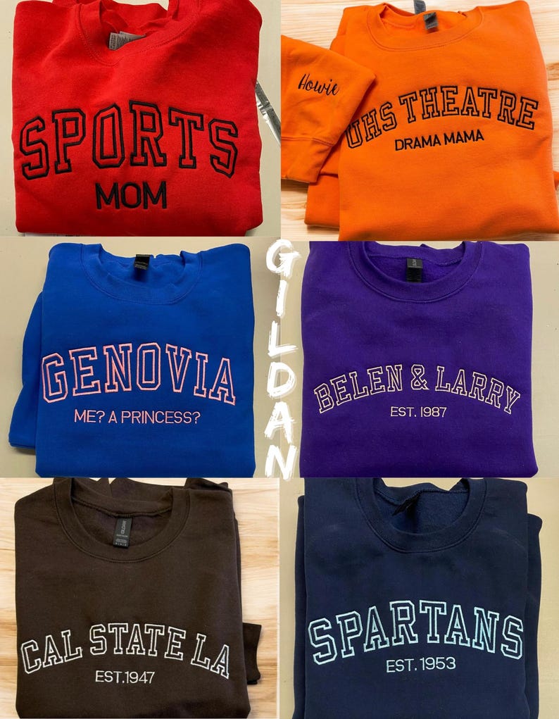May include: A collection of crewneck sweatshirts in various colors, each featuring embroidered text. The sweatshirts include phrases like "SPORTS MOM," "UHS THEATRE DRAMA MAMA," "GENOVIA ME? A PRINCESS?," "BELEN & LARRY EST. 1987," "CAL STATE LA EST.1947," and "SPARTANS EST. 1953."
