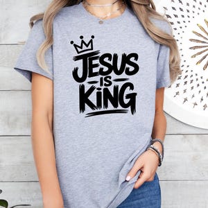 Pu&ograve; includere: T-shirt grigio athletic heather con la scritta nera "Jesus is King". Il design include una corona sopra la parola "Jesus". La maglietta a girocollo a maniche corte &egrave; realizzata in materiale morbido.