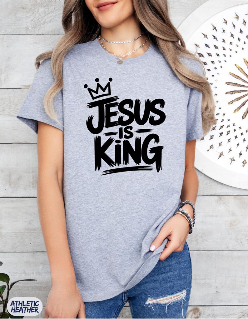 Pu&ograve; includere: T-shirt grigio athletic heather con la scritta nera "Jesus is King". Il design include una corona sopra la parola "Jesus". La maglietta a girocollo a maniche corte &egrave; realizzata in materiale morbido.
