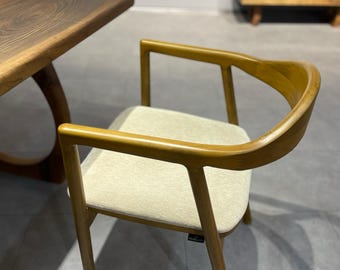 May include: A wooden dining chair with a light beige upholstered seat and a curved back. The chair has a natural wood finish and a simple, modern design.