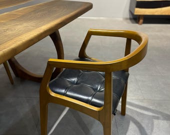 May include: A wooden chair with a black leather seat and a curved back. The chair is made of solid wood and has a natural finish.