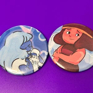 May include: Two round, colorful buttons featuring cartoon characters. One button has a light blue character with white accents, set against a blue background. The other button has a red-toned character with a brown headband, set against a blue background.