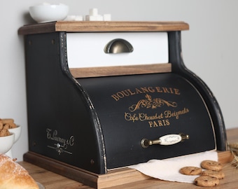 May include: A black and white wooden bread box with a roll-top door featuring the gold text BOULANGERIE, Cafe Chaud et Beignets, PARIS. The unit includes a top drawer with a bronze handle and a lower door with a white ceramic and bronze handle.