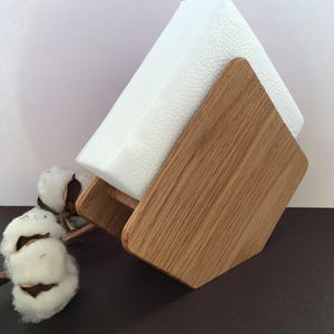 Puede incluir: Un servilletero de madera con un dise&ntilde;o geom&eacute;trico, que sostiene una pila de servilletas blancas. El soporte est&aacute; hecho de madera clara y tiene un patr&oacute;n de vetas natural. Una ramita de algod&oacute;n a&ntilde;ade un toque decorativo.