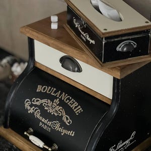 Puede incluir: Un juego de caja de pa&ntilde;uelos y pan negro y madera con el texto "Cafe Chaudet Beignets PARIS" y "BOULANGERIE Cafe Chaudet Beignets PARIS". El juego tiene una est&eacute;tica vintage con tiradores de metal y un caj&oacute;n blanco.