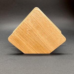 Puede incluir: Una pila de cuatro posavasos de madera con un acabado de veta de madera natural marr&oacute;n claro. Los posavasos son cuadrados con bordes biselados, dispuestos en forma de pir&aacute;mide. Los posavasos son de madera maciza.