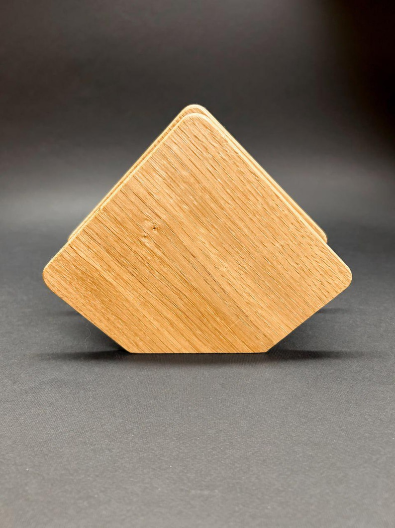 Puede incluir: Una pila de cuatro posavasos de madera con un acabado de veta de madera natural marr&oacute;n claro. Los posavasos son cuadrados con bordes biselados, dispuestos en forma de pir&aacute;mide. Los posavasos son de madera maciza.