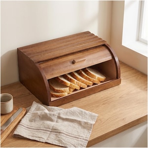 Könnte beinhalten: Ein mittelbrauner Brotkasten aus Holz mit einem Rolldeckel und einem kleinen Griff. Im Inneren des Kastens sind mehrere Scheiben Weißbrot in einer Reihe angeordnet. Der Brotkasten besteht aus horizontalen Holzlatten und ist oben gewölbt.