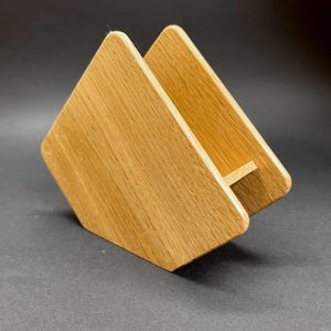 Puede incluir: Un servilletero de madera con un acabado de vetas naturales. El soporte est&aacute; construido con dos piezas de madera anguladas unidas en la base, creando una forma triangular. El soporte est&aacute; dise&ntilde;ado para sujetar servilletas en posici&oacute;n vertical.