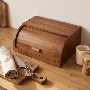 May include: A medium-brown wooden bread bin with a roll-top lid and a small horizontal handle. The rectangular container features horizontal slats across the curved top surface and a smooth, flat base, showcasing a natural wood grain finish.