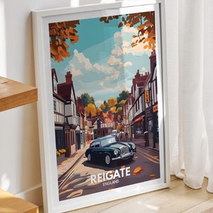 May include: A framed poster with a vintage illustration of a street scene in Reigate, England. The poster features a classic car driving down a street lined with buildings and trees. The text "Reigate, England" is printed at the bottom of the poster.