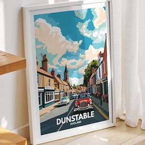 Puede incluir: Una impresión enmarcada de una ilustración vintage de una escena callejera en Dunstable, Inglaterra. La impresión presenta un cielo azul con nubes blancas, un coche rojo conduciendo por la calle y edificios a ambos lados de la calle. La impresión está enmarcada en un marco blanco.