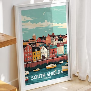 以下が含まれることがあります： 建物とボートのある海岸の町のカラフルなイラストが描かれた白い額縁のポスター。ポスターには「サウスシールド、イングランド」と書かれています。