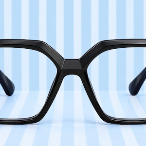 May include: Black eyeglasses with a thick, angular, geometric frame design. The glasses feature a prominent bridge and wide, square-shaped lenses. The temples are connected to the front frame with a distinct, blocky hinge mechanism on each side.