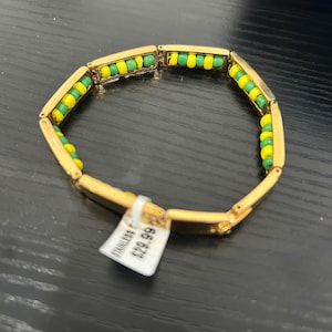 May include: Gold-toned bracelet with alternating green and yellow beads. The bracelet is made of stainless steel and has a rectangular link design. The beads are small and evenly spaced.