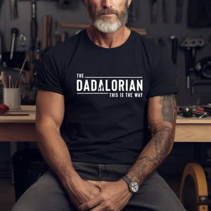 Könnte beinhalten: Ein schwarzes T-Shirt mit weißem Text, der "The Dadalorian - This is the Way" lautet.