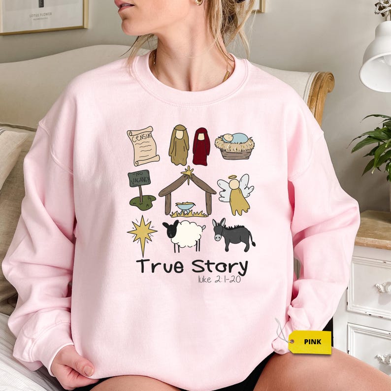 a woman sitting on a bed wearing a pink sweatshirt