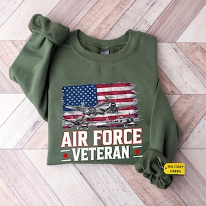 May include: A green sweatshirt with a distressed American flag and a vintage airplane graphic. The text "AIR FORCE VETERAN" is printed in white below the graphic.