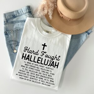 a white t - shirt with a cross and a hat on top of it
