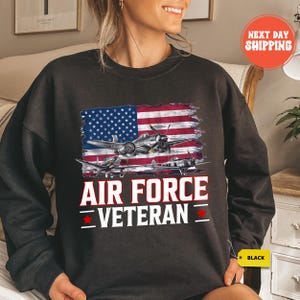 a woman sitting on a bed wearing an air force veteran sweatshirt