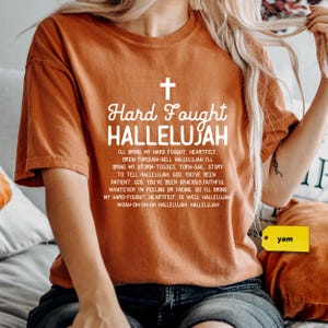 a woman sitting on a bed wearing a t - shirt with a cross on it