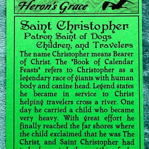 May include: Green card with black text about Saint Christopher, Patron Saint of Dogs, Children, and Travelers. The text explains that the name Christopher means "Bearer of Christ" and that the "Book of Calendar Feasts" refers to Christopher as a legendary race of giants with a human body and canine head. The text continues to describe a legend about Saint Christopher carrying a child across a river.
