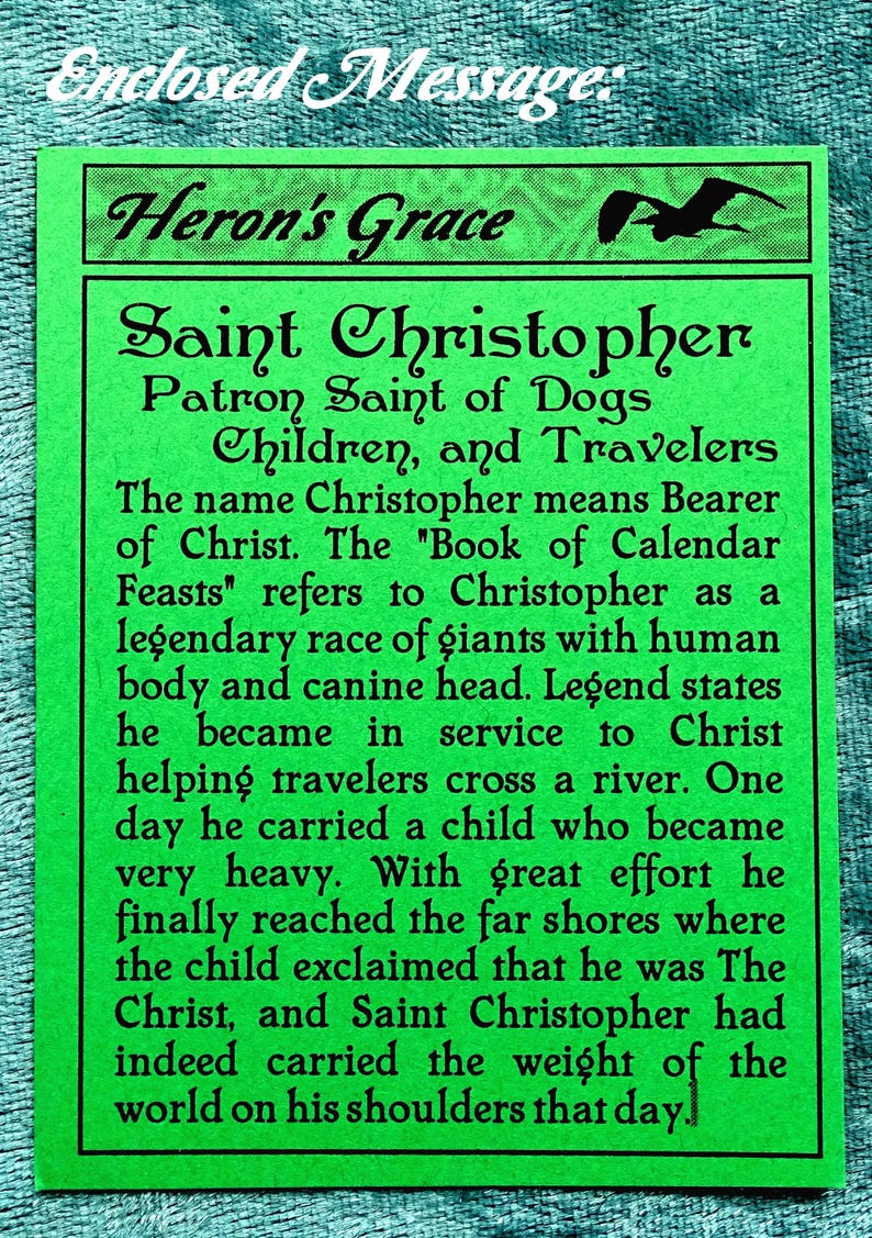 May include: Green card with black text about Saint Christopher, Patron Saint of Dogs, Children, and Travelers. The text explains that the name Christopher means "Bearer of Christ" and that the "Book of Calendar Feasts" refers to Christopher as a legendary race of giants with a human body and canine head. The text continues to describe a legend about Saint Christopher carrying a child across a river.