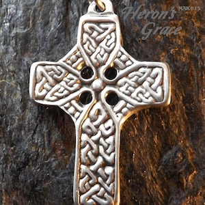 May include: Silver Celtic knot cross pendant with intricate details and four open circles. The pendant is hanging on a black cord.