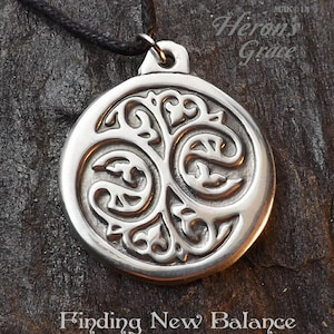 May include: Silver pendant necklace featuring a detailed tree of life design. The pendant is round and has a black cord.