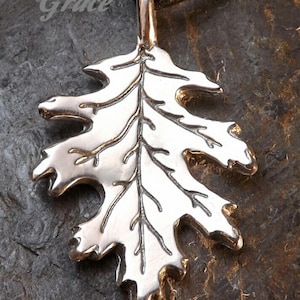 May include: A silver pendant in the shape of a red oak leaf. The leaf is detailed with veins and has a smooth, polished finish.