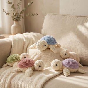 May include: A collection of handmade crochet turtle toys in various pastel colors, including blue, green, pink, and purple. The turtles are arranged on a cream-colored blanket and sofa, creating a cozy and inviting scene.