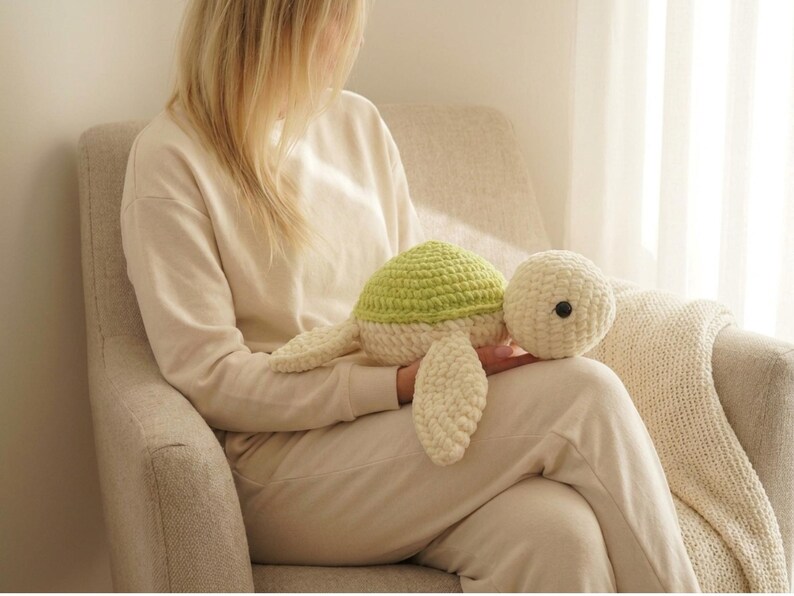 May include: A handmade crochet turtle plush toy. The turtle has a light green shell, cream-colored body, and a black button eye. The turtle is a soft, cuddly toy, perfect for children or as a decorative item. The turtle is approximately 12 inches long.